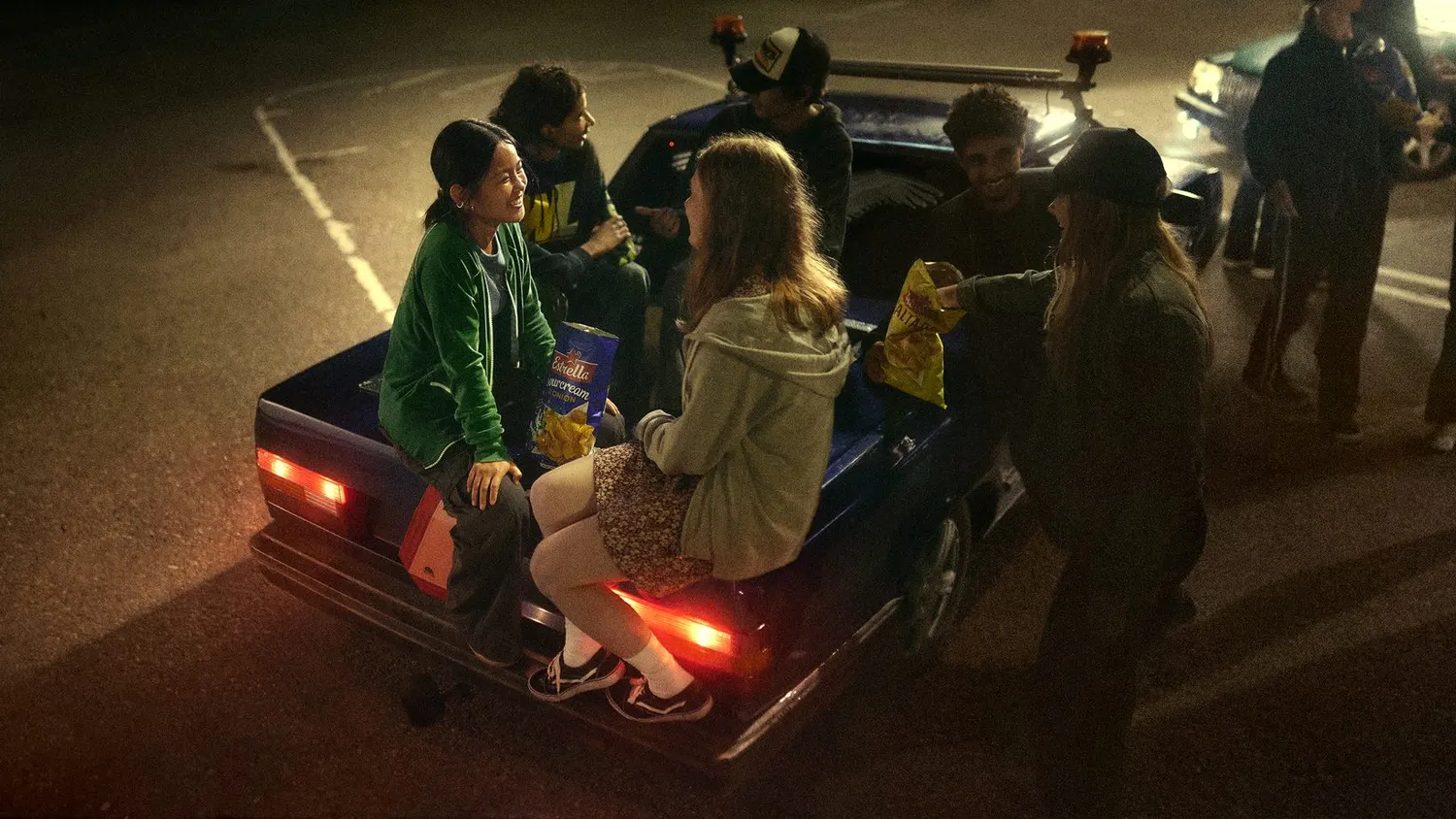 Teenagers hanging out on a car at night, from Estrella's campaign Låt stunderna börja